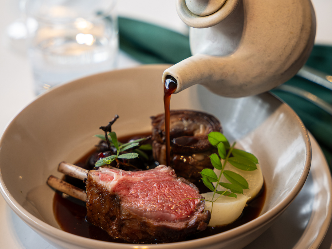 Sauce being poured onto a lamb rib dish designed by Collective Hospitality for business events.
